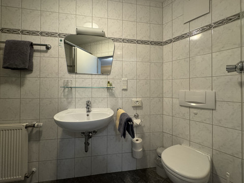 Hotel Garni Alt Refrath - Badezimmer 1 Ein hell gefliestes Bad mit Wandspiegel, Waschbecken und einem Haken neben einem Handtuchhalter.