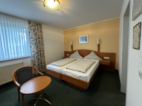 Hotel Garni Alt Refrath - Doppelzimmer 2 Ein gemütliches Hotelzimmer mit zwei Einzelbetten, einem runden Tisch und einem Stuhl in warmen Farben.