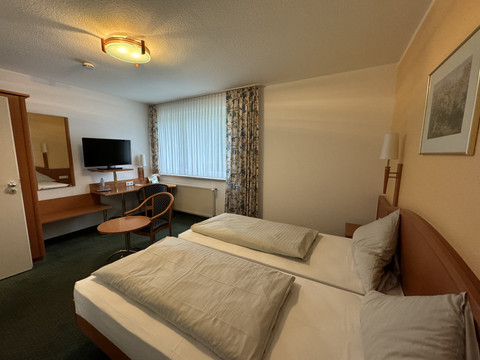 Hotel Garni Alt Refrath - Doppelzimmer 2 Zweibettzimmer mit TV, Schreibtisch und gemütlichen Sitzgelegenheiten, große Fenster mit Vorhängen.