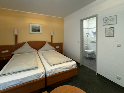 Hotel Garni Alt Refrath - Doppelzimmer 2  Das Bild zeigt ein Doppelzimmer mit zwei Einzelbetten und einem angrenzenden Badezimmer.
