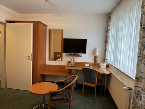 Hotel Garni Alt Refrath - Doppelzimmer 2 Ein gemütlich eingerichtetes Hotelzimmer mit Tisch, zwei Stühlen, Schreibtisch, TV und großem Fenster.