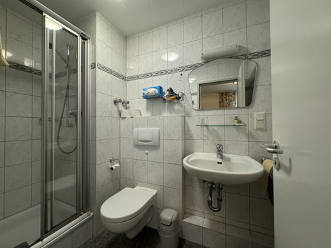 Hotel Garni Alt Refrath - Badezimmer 2 Ein kompaktes, weiß gefliestes Badezimmer mit Dusche, Waschbecken und WC in neutralem Design.