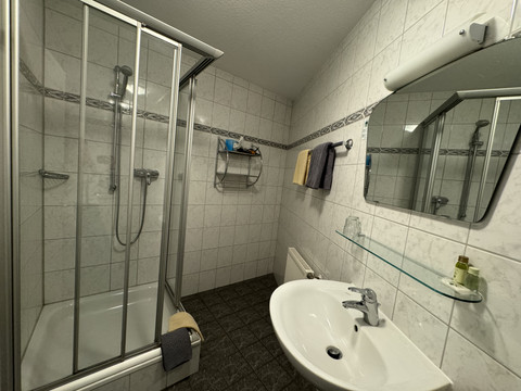 Hotel Garni Alt Refrath - Badezimmer 1 Ein modern gefliestes Badezimmer mit Dusche, Waschbecken und Spiegel. Handtücher und Pflegeartikel sind vorhanden.