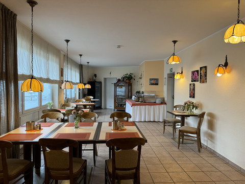 Hotel Garni Alt Refrath - Innenansicht Essbereich  Gemütlicher Frühstücksraum mit Holzmöbeln, großen Fenstern und dekorativen Lampen, einladend und hell.