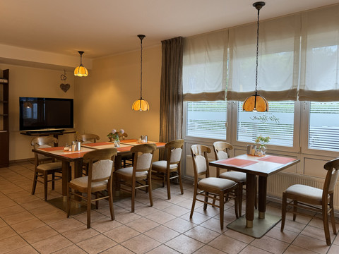 Hotel Garni Alt Refrath - Innenansicht Essbereich  Gemütlicher Speiseraum mit hölzernen Tischen und Stühlen, dekorativen Lampen und großen Fenstern.