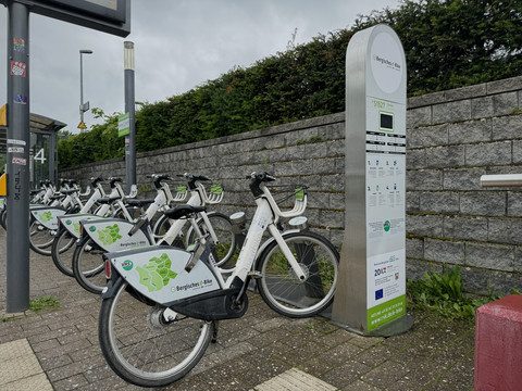 E-Bike Verleihstation  Fahrradverleihstation mit weißen Leihrädern vor einer Steinmauer, bereit zur Nutzung.