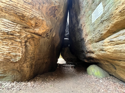 Schmale Felsformation mit sandfarbenen, strukturierten Wänden und einem kleinen Durchgang; ein Schild ist an der rechten Wand angebracht.