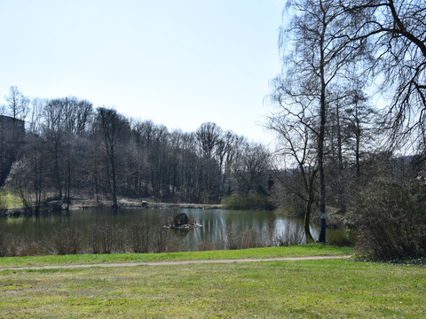 Heilteich  Ein idyllischer See mit Uferweg, umgeben von kahlen Bäumen unter klarem Himmel.