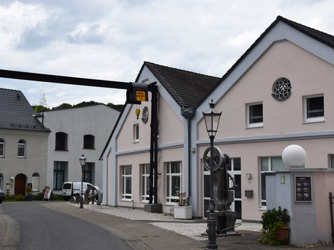 Hoffnungsthaler Hammer <p>Modernisiertes, rosafarbenes Gebäude in Rösrath mit markanten Kunstinstallationen im Vordergrund.</p>