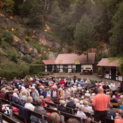 Piumer Bauerntheater - Publikum.jpg Eine große Menschenmenge sitzt auf Holzbänken vor einer Bühne in einem natürlichen Amphitheater.