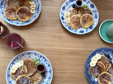 Kaffeepause - Ansicht Pancakes Pfannkuchen mit Puderzucker und Bananenscheiben, begleitet von Sirup und Fruchtsaft auf Holztisch.