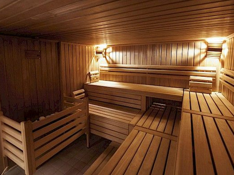Sauna.jpg Holzverkleidete Sauna mit zweistufigen Bänken und warmer Beleuchtung, die Komfort und Entspannung bietet.