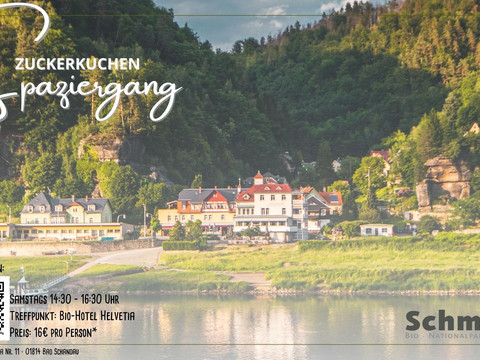 Zuckerkuchen-Spaziergang Eine malerische Flusslandschaft mit Gebäuden im Vordergrund, umgeben von grünen, bewaldeten Hügeln.