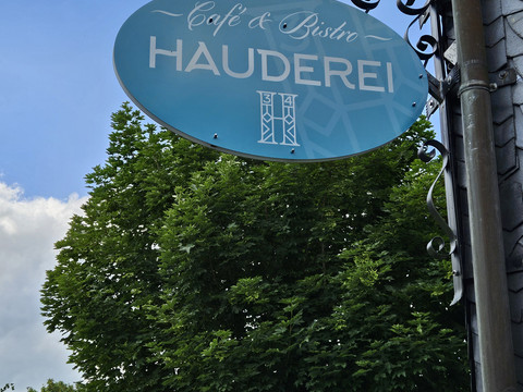 Hauderei Café & Bistro Ein rundes, blaues Schild mit der Aufschrift "Café & Bistro Hauderei" hängt an einer Halterung.