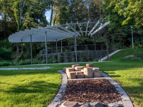 Kurpark in Reichshof-Eckenhagen Barfusspfad Ein moderner, offener Pavillon mit Holzbänken umgeben von grüner Rasenfläche und Bäumen.