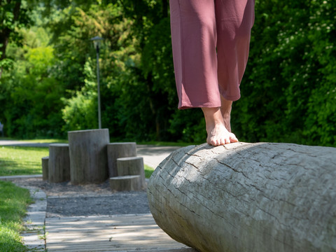 Kurpark in Reichshof-Eckenhagen Barfusspfad Person balanciert barfuß auf einem liegenden Baumstamm in einem grünen Park.