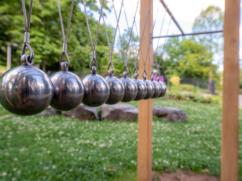 Kurpark in Reichshof-Eckenhagen Sinneselemente Neun symmetrisch aufgehängte Kugeln eines Newton-Pendels aus Metall im Freien vor grüner Landschaft.
