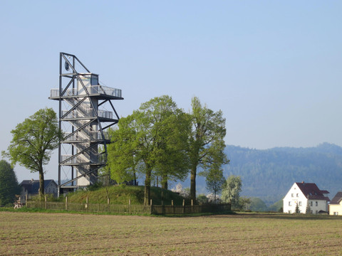 Aussichtsturm in Rathmannsdorf Aussichtsturm neben einem Feld mit zwei Häusern, bewaldete Hügel im Hintergrund.