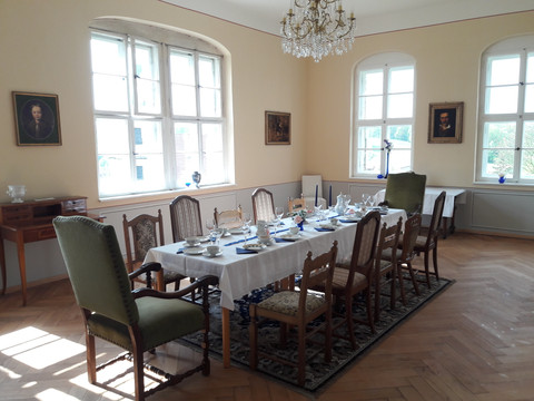 Feestelijke tafel in het kasteel Elegantes Esszimmer mit gedecktem Tisch für acht Personen, umgeben von antiken Stühlen, Kronleuchter und Porträts an den Wänden, helle Atmosphäre.