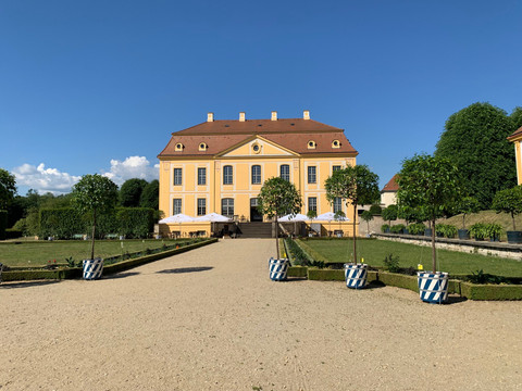Uitzicht op het kasteel Gelbes Barockgebäude des Barockgarten Großsedlitz mit rotem Dach, umgeben von gepflegtem Garten und Bäumen in blau-weißen Töpfen, unter klarem blauem Himmel.Yellow baroque building of the Grosssedlitz Baroque Garden with a red roof, surrounded by well-tended gardens and trees in blue and white pots, under a clear blue sky.Žlutá barokní budova barokní zahrady Grosssedlitz s červenou střechou, obklopená udržovanými zahradami a stromy v modrých a bílých květináčích, pod jasně modrou oblohou.Żółty barokowy budynek Ogrodu Barokowego Grosssedlitz z czerwonym dachem, otoczony zadbanymi ogrodami i drzewami w niebieskich i białych donicach, pod czystym błękitnym niebem.Geel barokgebouw van de Grosssedlitz Baroque Garden met een rood dak, omringd door goed onderhouden tuinen en bomen in blauwe en witte potten, onder een strakblauwe hemel.Edificio barocco giallo del Giardino Barocco di Grosssedlitz con tetto rosso, circondato da giardini ben curati e alberi in vasi blu e bianchi, sotto un cielo azzurro e limpido.