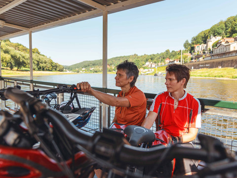 Op de veerboot naar Königstein Zwei Personen in Sportkleidung sitzen mit Fahrrädern auf einer Fähre, umgeben von Flusslandschaft und sonnigem Wetter.Two cyclists on the Königstein ferryDva cyklisté na přívozu KönigsteinTwee fietsers op de veerboot naar KönigsteinDwie osoby w strojach sportowych siedzą na promie z rowerami, otoczone scenerią rzeki i słoneczną pogodą.Due persone in abbigliamento sportivo siedono su un traghetto con le biciclette, circondate dal paesaggio fluviale e dal tempo soleggiato.