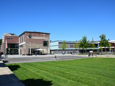 Steinmüllergelände <p>Ein Platz mit alten Backsteingebäuden, modernen Fassaden und einem grünen Rasen bei Sonnenschein.</p>