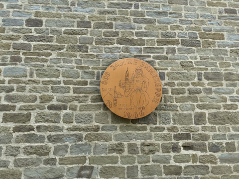 St. Lucia Rundes Sandsteinrelief an einer Mauer erinnern an 800 Jahre Jännerwein mit Inschrift und Burgmotiv.