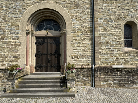 St. Lucia  Steinernes Kirchenportal mit prunkvoller Schmiedeeisentür, flankiert von Blumen und Treppenstufen.