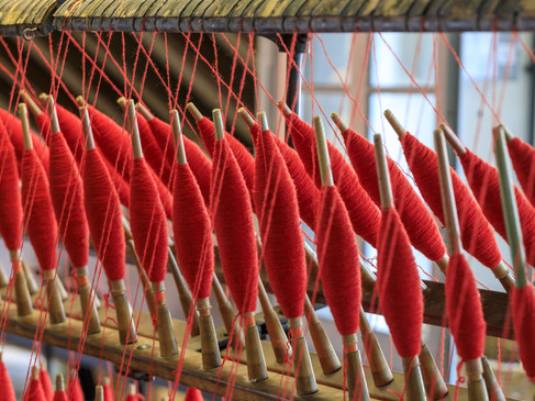 Rote Wollspulen auf traditionellen Spindelrahmen in einer alten Weberei angeordnet.