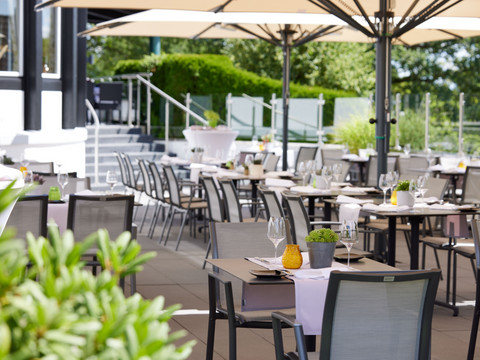 Derichsweiler Hof Sonnige Terrasse eines Restaurants mit gedeckten Tischen und modernen Stühlen unter großen Schirmen.