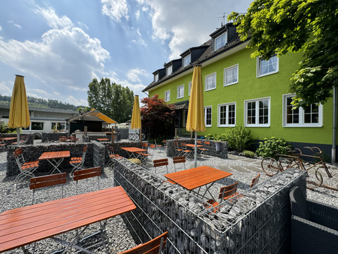 Haus Thal - Ansicht Außenbereich Außenansicht eines Restaurants mit grüner Fassade, roten Tischen, gelben Schirmen und Kiesboden.