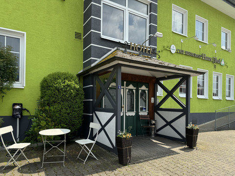 Haus Thal - Ansicht Eingangsbereich Eingang eines grün gestrichenen Hotels mit rustikalem Vordach und zwei Stühlen vor der Tür.