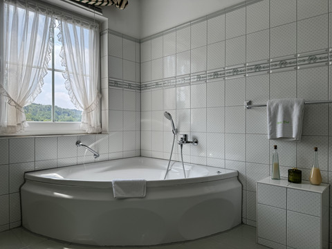 Haus Thal - Zimmer 2 - Badezimmer Badezimmer mit einer großen, weißen Eckbadewanne unter einem Fenster, sanft einfallendes Tageslicht.