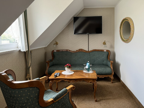 Haus Thal - Zimmer 2 - Sitzbereich Gemütliches Hotelzimmer mit Schrägdach und Retro-Möbeln, bestehend aus einem Sofa, Sessel, Tisch und TV.