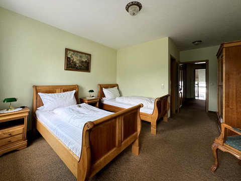 Haus Thal - Zimmer 1 Zwei rustikale Einzelbetten aus Holz in einem gemütlichen, hellgrünen Zimmer mit Teppichboden.