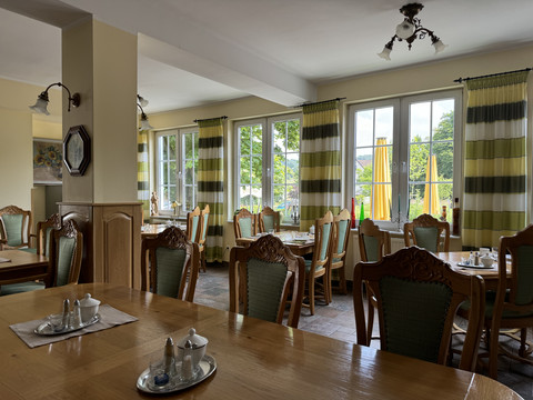 Haus Thal - Ansicht Restaurant Innenbereich Heller Gastraum mit eleganten Holzmöbeln, großen Fenstern und Blick auf grüne Landschaft und Sonnenschirme.