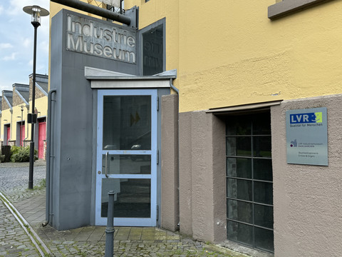 LVR-Industriemuseum Eingang zum Industriemuseum mit gelber Fassade, blauem Türrahmen und LVR-Besucherschild rechts.