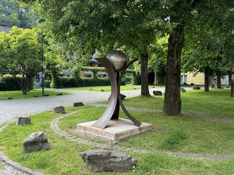 LVR-Industriemuseum Gelände Skulptur mit einer metallischen Kugel auf drei geschwungenen Stützen in einem grünen Park.