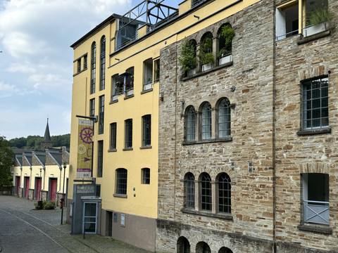 LVR-Industriemuseum Historisches Gebäude mit gelber und steinerner Fassade, dahinter eine Kirche vor bedecktem Himmel.