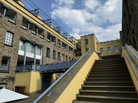 LVR-Industriemuseum Gelbes Gebäude mit Stein- und Glaselementen, Treppe im Vordergrund, blauer Himmel mit Wolken.