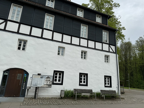 Papiermuseum Fachwerkhaus mit weißer Fassade, schwarzen Balken, drei Stockwerken, neben Kasse, Bänke im Vordergrund.