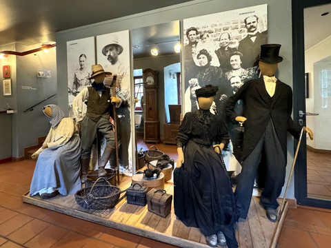 Bergisches Museum für Bergbau, Handwerk und Gewerbe Mehrere Schaufensterpuppen in traditionellen Trachten, umgeben von Körben, in einem Ausstellungsraum.