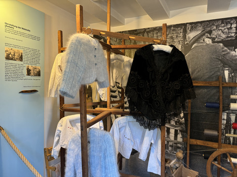 Bergisches Museum für Bergbau, Handwerk und Gewerbe Alte Webstuhl-Szene in einem Museum mit historischen Kleidungsstücken und gewobenen Textilien.