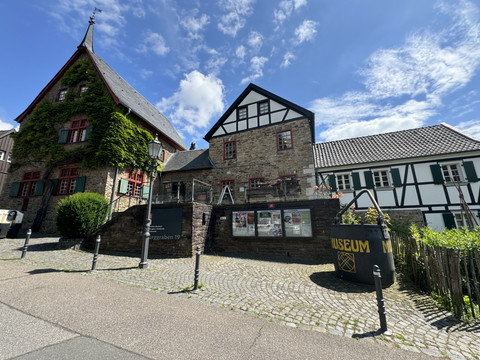 Bergisches Museum für Bergbau, Handwerk und Gewerbe Historisches Fachwerkgebäude mit grünem Efeu bewachsen, unter blauem Himmel. Pflastersteine vorne.