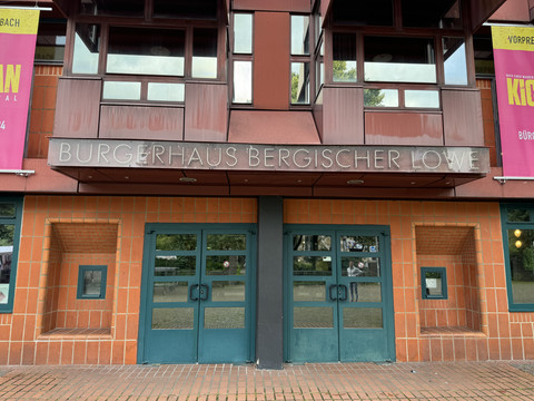 Bergischer Löwe Eingang des Bürgerhauses Bergischer Löwe mit vier modern gestalteten Glastüren und roter Fassade.