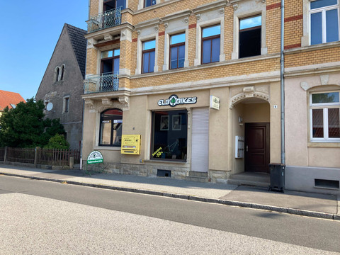 Elbbikes bike shop in Pirna Bicycle store in an old building with a yellow brick façade, next to a gray house. A sign saying "bicycle service" stands in front of the store.