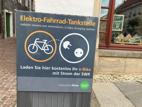 Pirna oplaadpunt voor e-bikes Ein Schild für eine Elektro-Fahrrad-Tankstelle mit Piktogrammen von Fahrrad und Stecker, bietet kostenloses Laden von E-Bikes an.