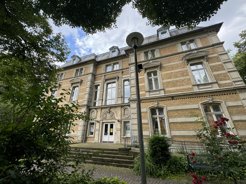 Kunstmuseum Villa Zanders Historisches Backsteingebäude mit verzierten Fassaden, umgeben von grünen Bäumen und blühenden Pflanzen.