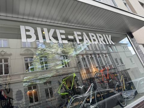 Bike-Fabrik Fahrradgeschäft mit modernen Bikes im Schaufenster, reflektierende Altbaufassaden im Glas.