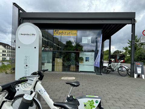 E-Bike Verleihstation Fahrradstation mit E-Bikes und Ladestation vor einem modernen Gebäude mit großen Glasfenstern.